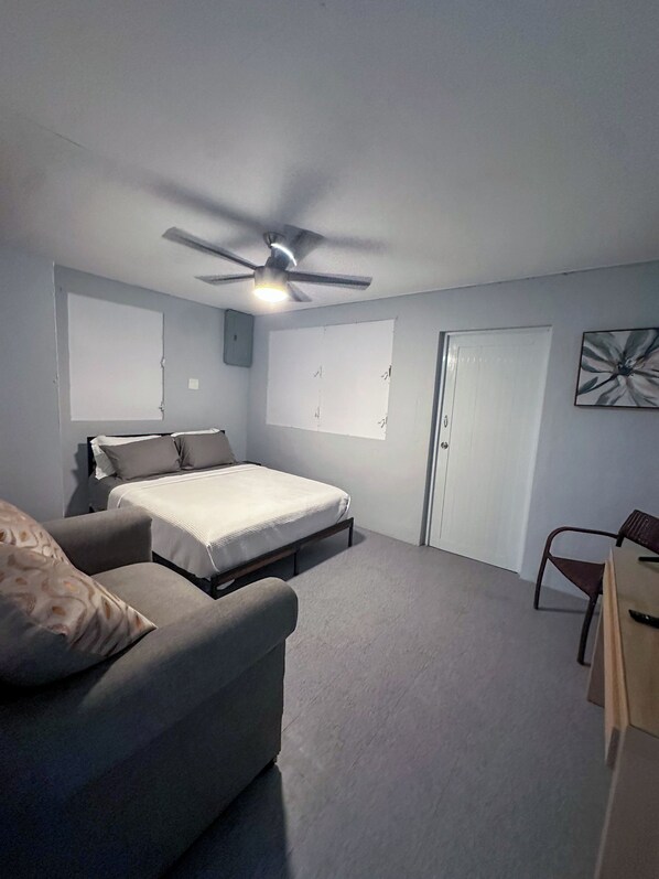 Un dormitorio con cama, una silla, un escritorio, un ventilador de techo y una puerta.
