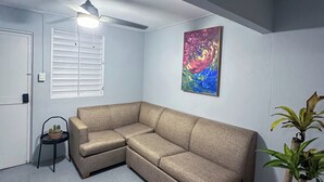 A corner room with a beige sectional sofa, a ceiling fan, a potted plant, and a painting on the wall.