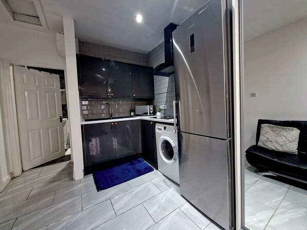 A compact kitchen with a built-in washing machine, a refrigerator, and a microwave.