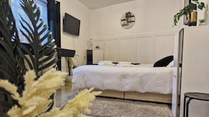 Moderni hotellihuone, jossa on suuri sänky, taulutelevisio, pieni huonekasvi ja koristeellinen seinäelementti.