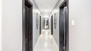 Un long couloir étroit, bordé de portes en bois sombre de part et d’autre, qui mène à une pièce lumineuse et bien éclairée au bout.