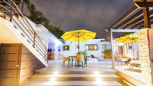 Un espace aménagé au bord de la piscine, avec des marches menant à un espace de détente couvert, agrémenté de parasols jaunes et de mobilier d’extérieur.