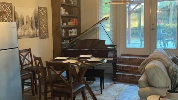 Tunnelmallinen ruokailutila, jossa on puutuolit ja piano, valkoinen sohva sekä keittiö, jossa on jääkaappi.