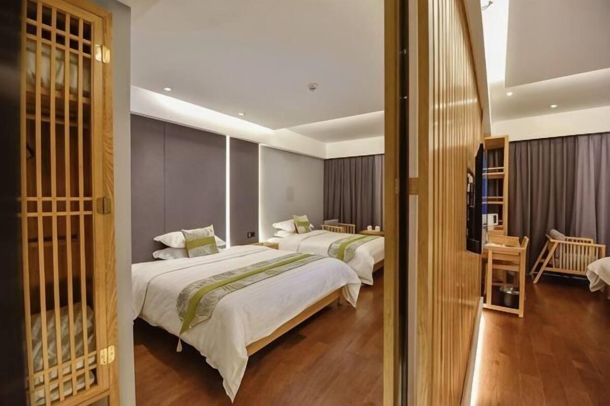 A hotel room with two beds, a wooden chair, a small table, and a large mirror.