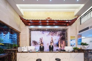 Zona de recepción de un hotel con mostrador, dos recepcionistas, una gran pantalla digital y un diseño arquitectónico tradicional.