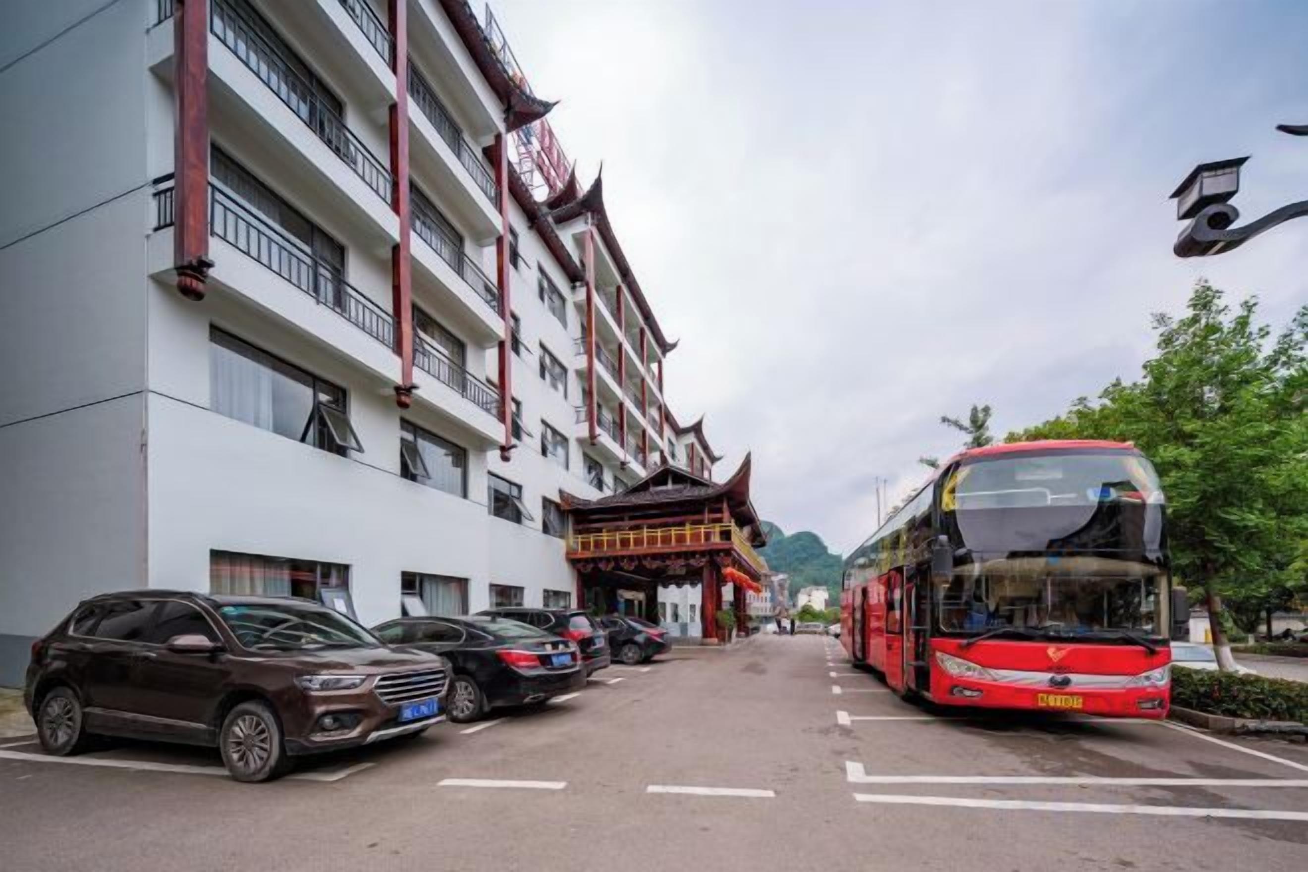 A multi-story building with a traditional architectural style, a red double-decker bus parked in front, and several cars parked along the street.
