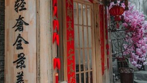 Un edificio de madera tradicional con letrero, faroles rojos y una planta en maceta.