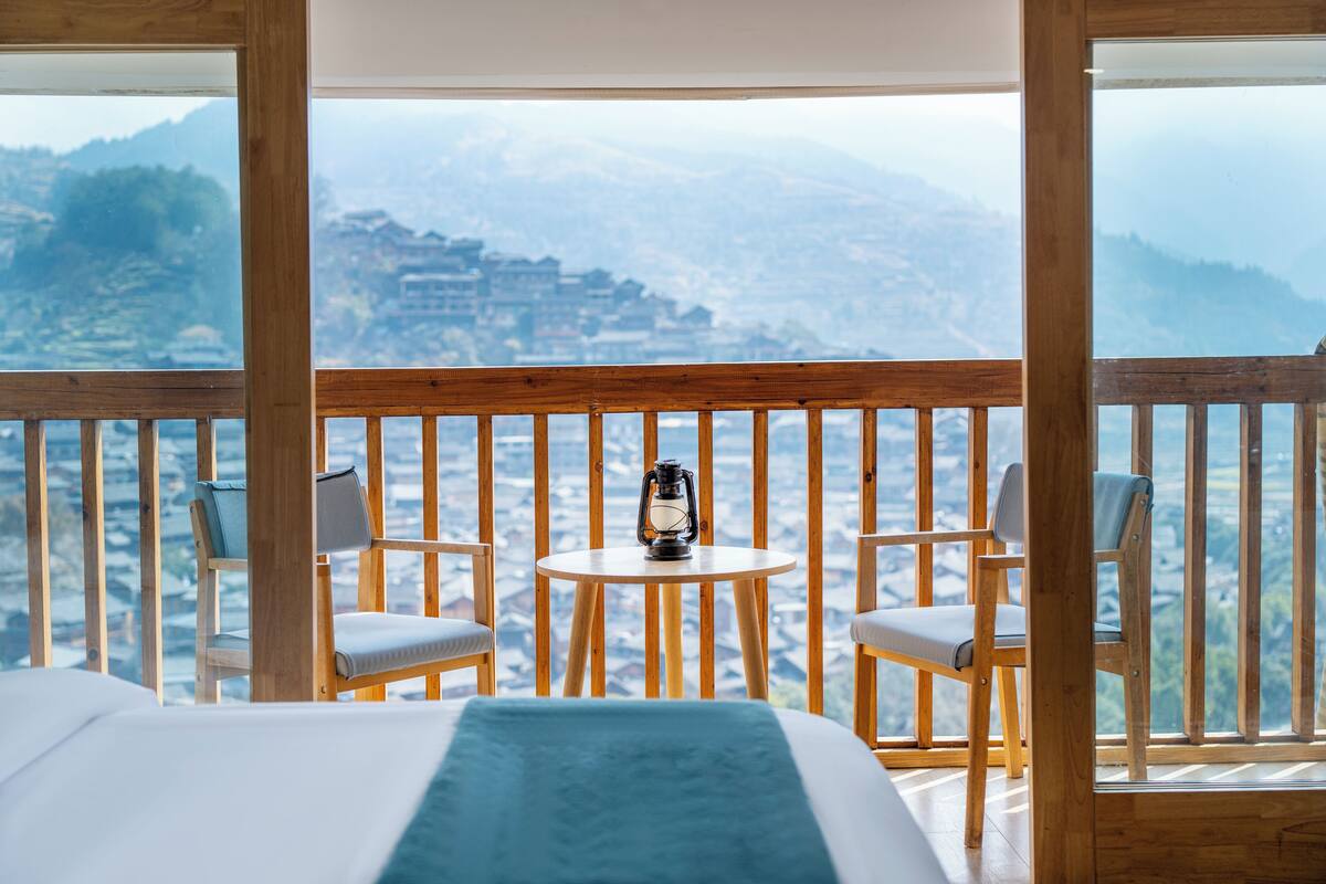 A balcony with a bed, two chairs, and a table with a lantern.