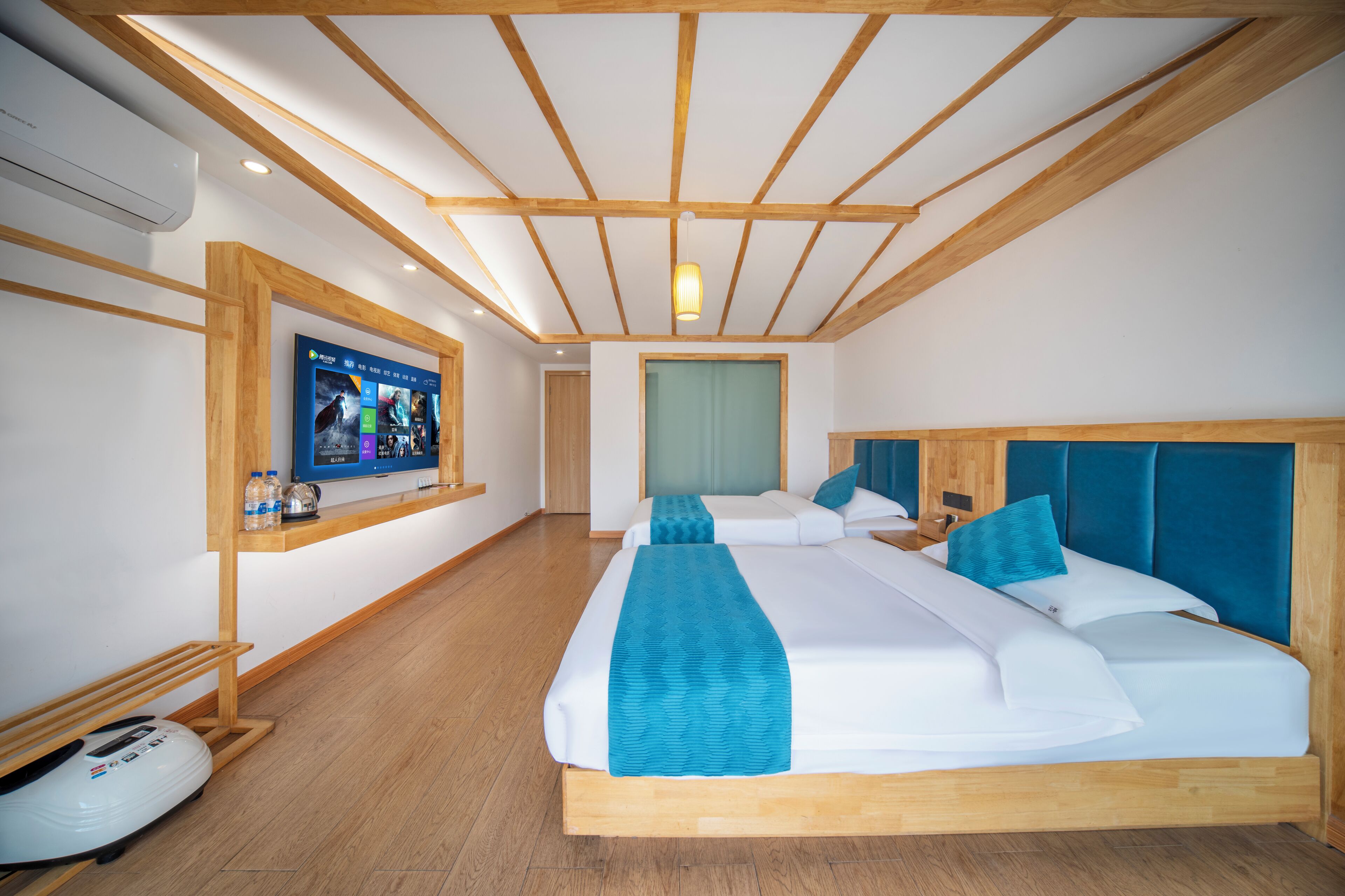 A hotel room with two beds, wooden beams on the ceiling, a TV on the wall, and a luggage trolley.