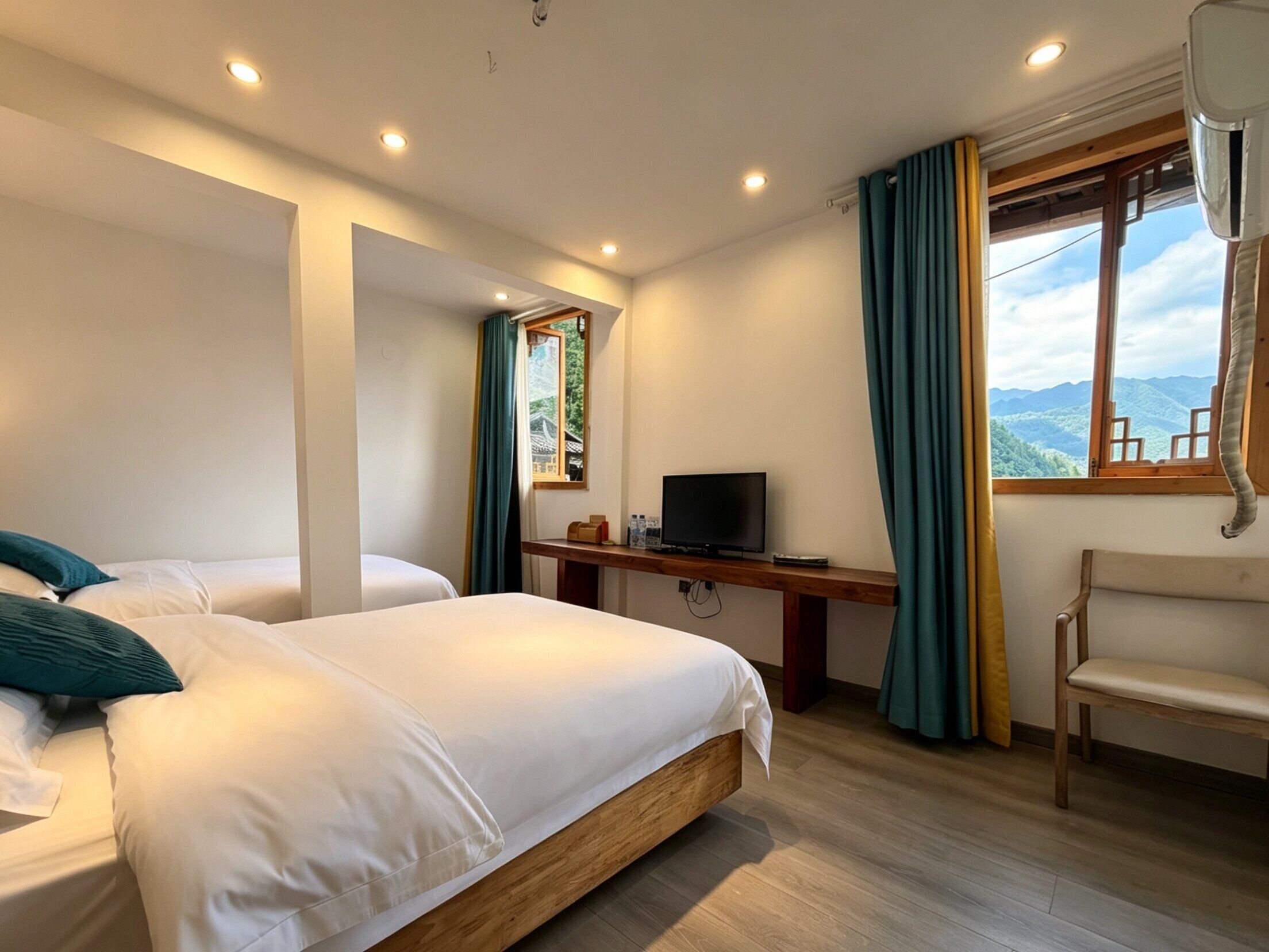 Hotelkamer met twee bedden, een bureau met een televisie, een stoel en een raam met uitzicht op bergen.