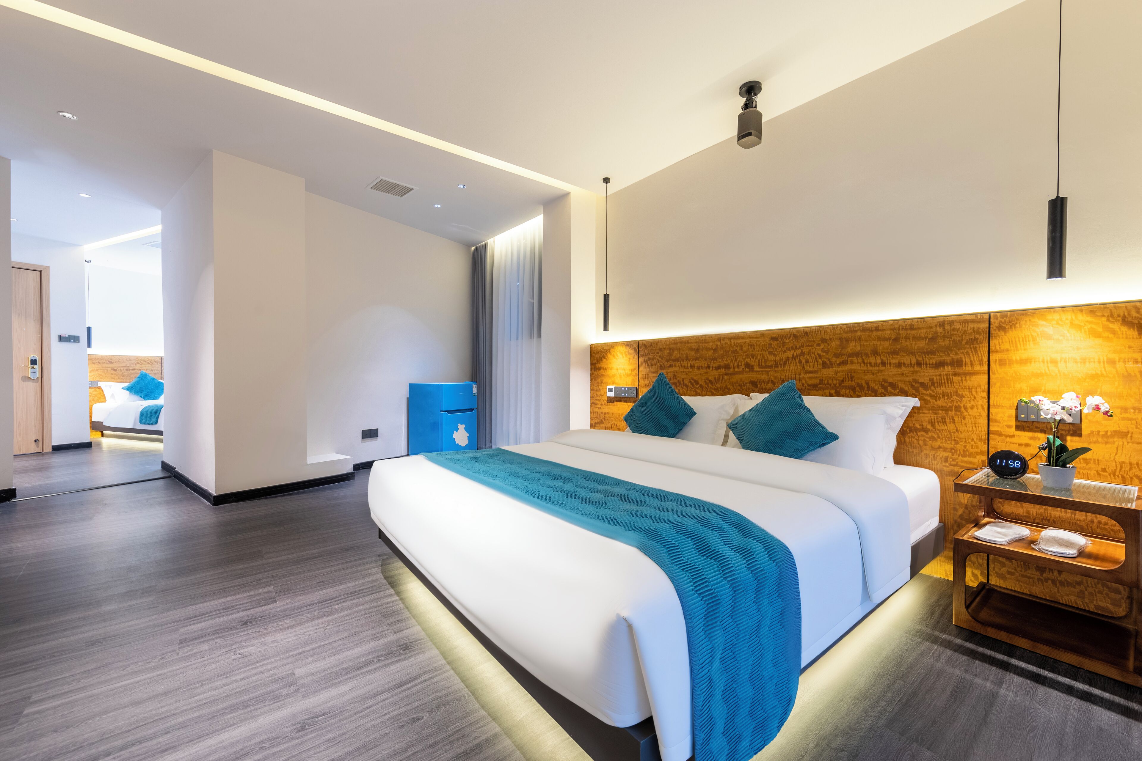 Una camera d'albergo moderna con un letto grande, una testiera in legno, un comodino con una sveglia e un tavolino da notte con una lampada.