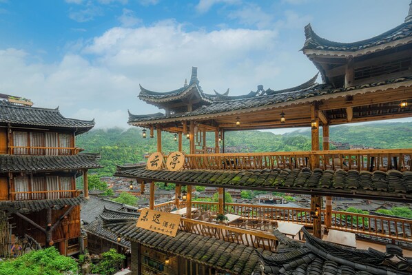 A traditional multi-story building with wooden balconies and tiled roofs, featuring a restaurant area with tables and chairs. - Xijiang Yunting Light Luxury Panoramic (Qiandongnan)