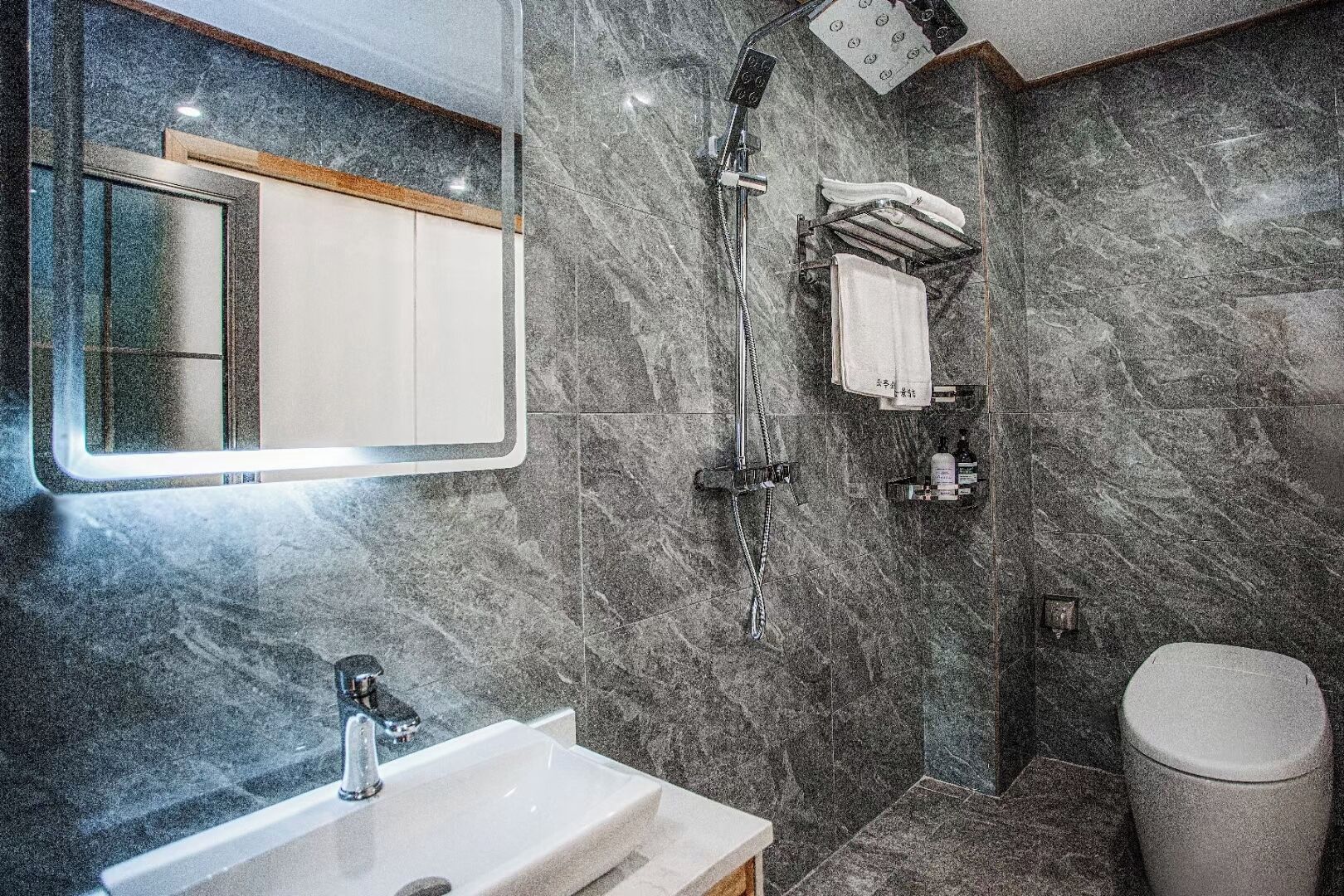 A modern bathroom with a marble wall, a sink, a toilet, and a shower.