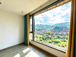 Una habitación con un gran ventanal, piso de madera y vista a un paisaje urbano con edificios y zonas verdes.