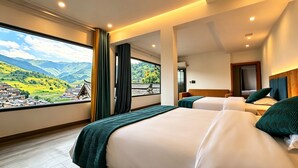 Habitación de hotel con dos camas, un ventanal con vistas a un pueblo y montañas, y una decoración interior moderna.