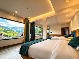 Habitación de hotel con dos camas, un ventanal con vistas a un pueblo y montañas, y una decoración interior moderna.