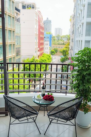 A balcony with two black wire chairs, a glass table, a bottle of wine, and a bouquet of red roses.