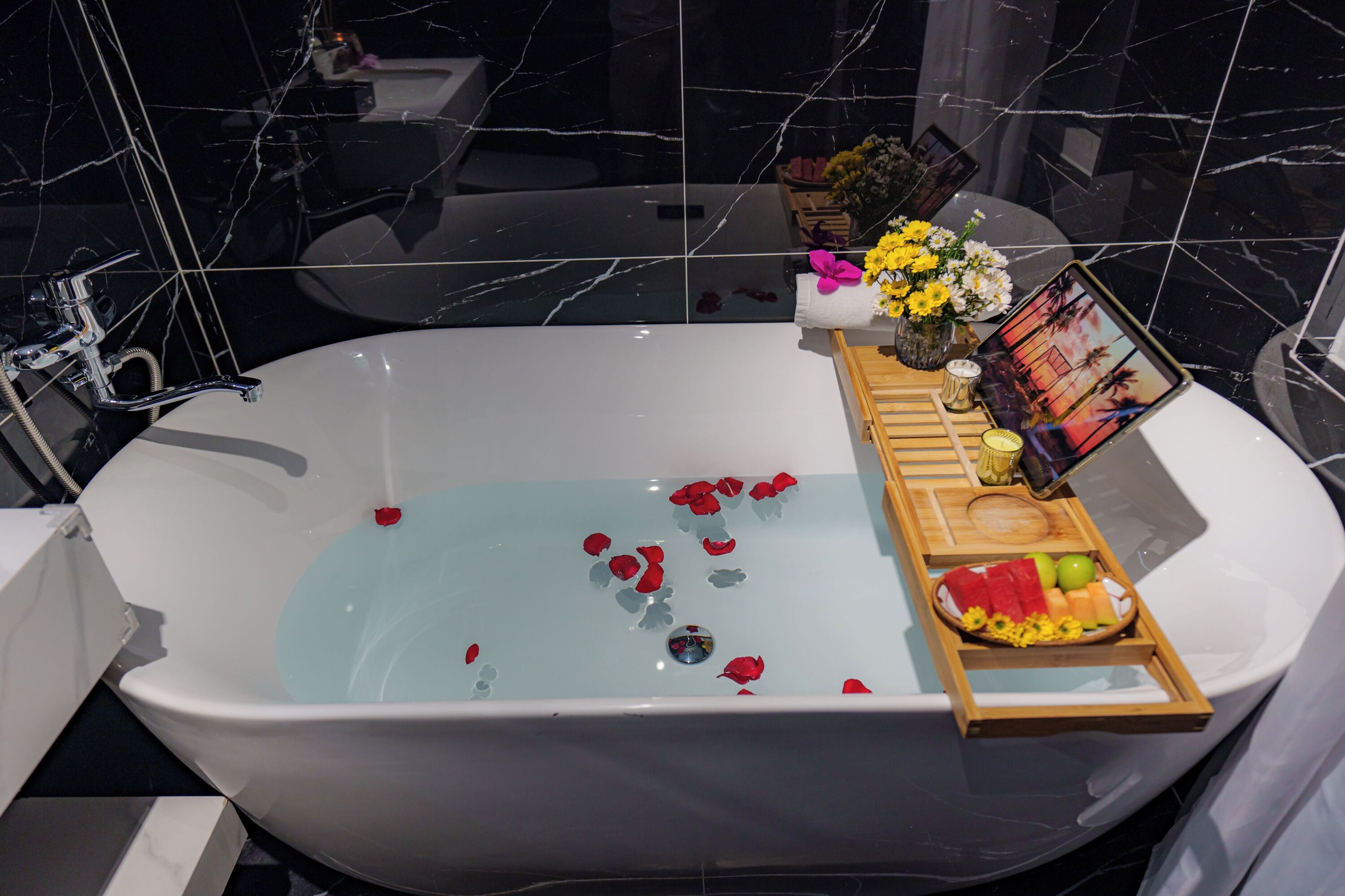 Ein modernes Badezimmer mit einer freistehenden Badewanne, einer Ablage mit Früchten und Blumen sowie einem gerahmten Bild an der Seite.