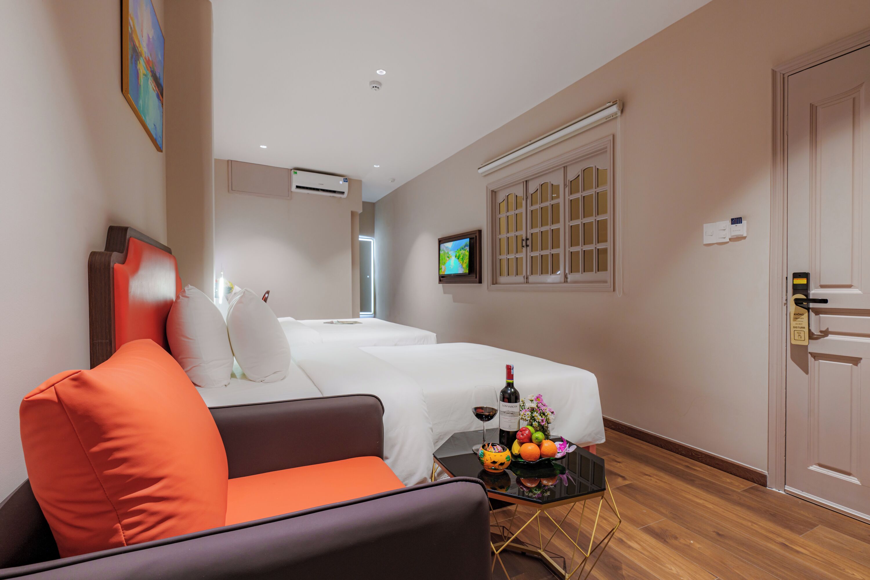 Una habitación de hotel con cama, sofá, una mesita con una botella de vino y un televisor en la pared.