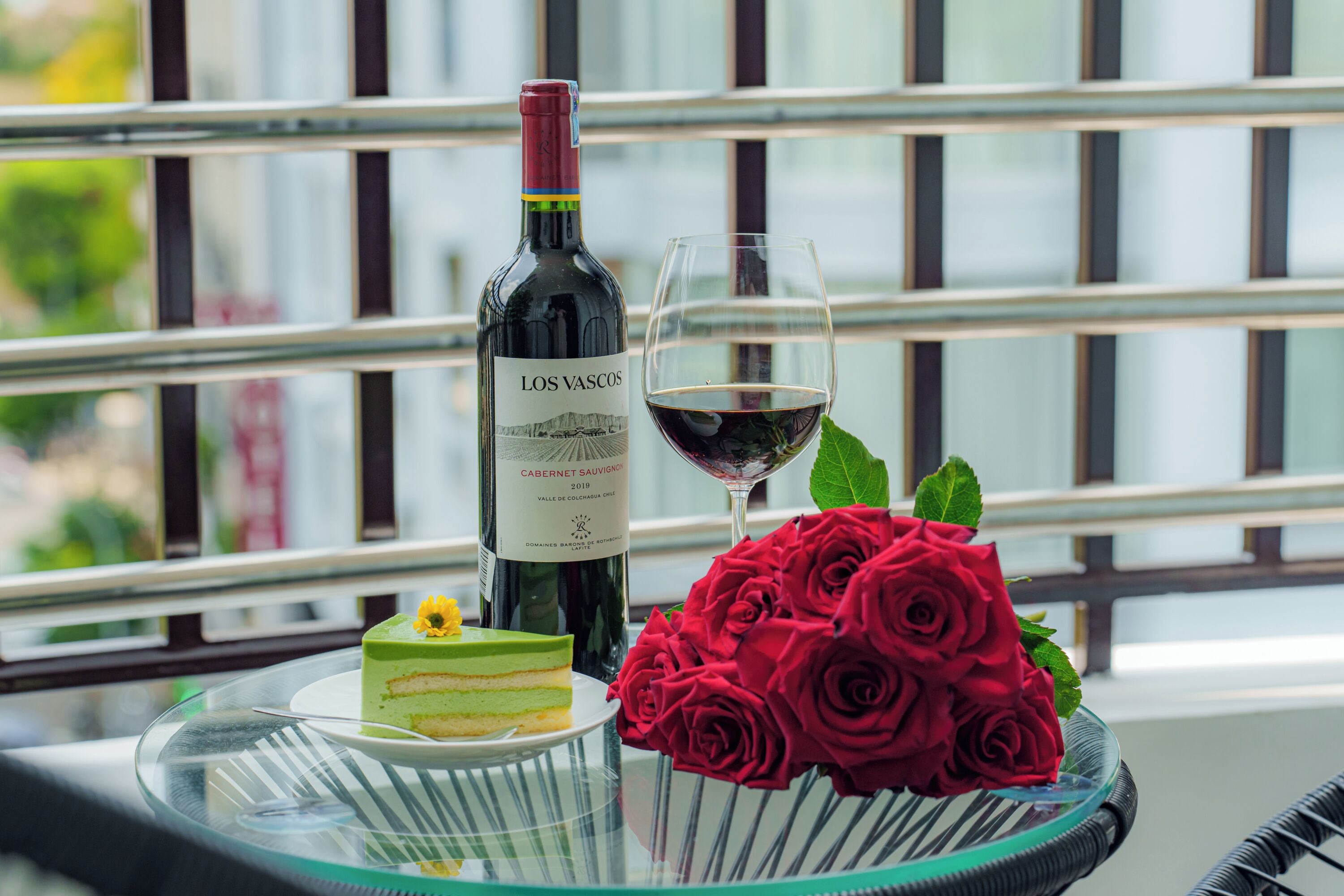 Una mesa de cristal con una botella de vino, una copa de vino y un pastel decorado con rosas.