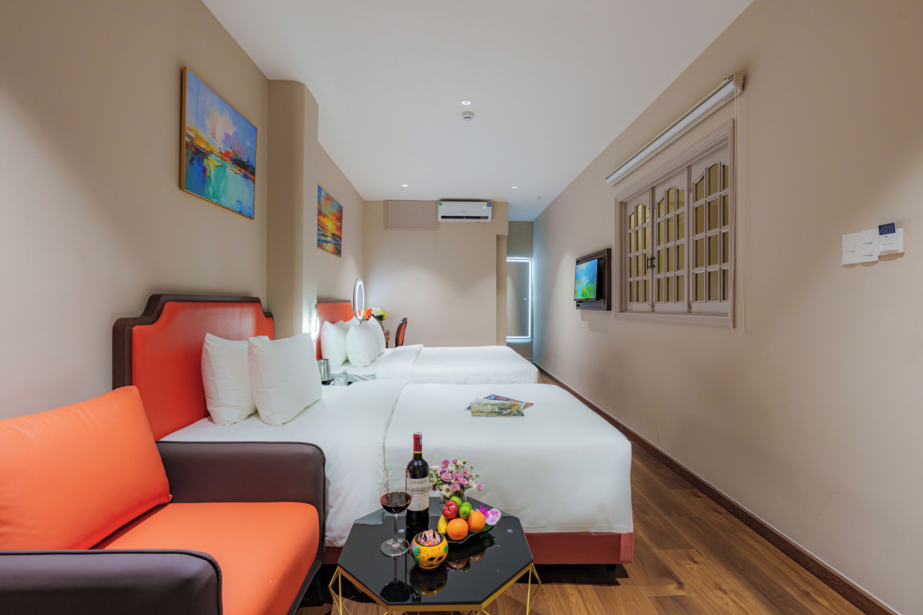 Ein Hotelzimmer mit Bett, einer Sitzecke, einem kleinen Tisch mit einer Weinflasche, einer Obstschale und einem Fernseher an der Wand.