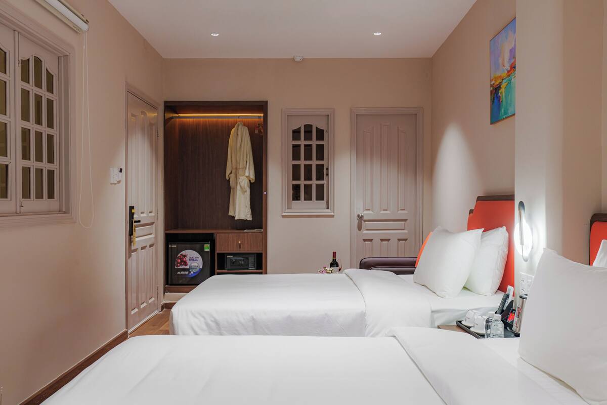Habitación de hotel con dos camas, un televisor, un minibar y una bata colgada en la puerta.