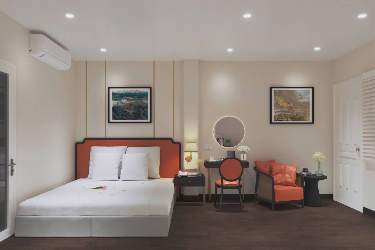 Habitación de hotel con una cama, un escritorio con silla, un espejo redondo y dos cuadros en la pared.