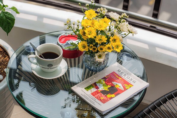 A glass table with a cup of coffee, a vase of yellow flowers, and a magazine on it.