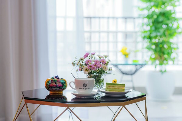 A table with a white cup, a vase with flowers, and a slice of cake.