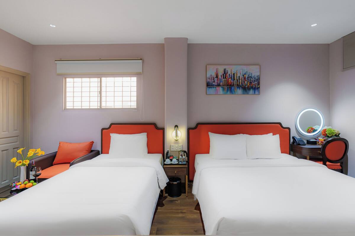 Habitación de hotel con dos camas, una ventana, un cuadro, un espejo y una mesita con un florero.