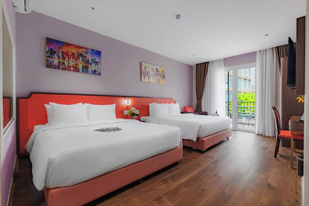 Habitación de hotel con dos camas, cabecera roja, un cuadro, ventana con cortinas y balcón.