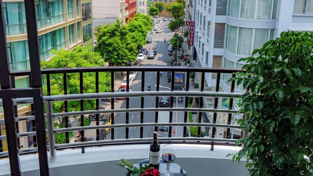 A balcony with two chairs, a table with a bottle of wine, a glass, and a cake. - Salute Saigon Hotel and Spa (Ho Chi Minh City)