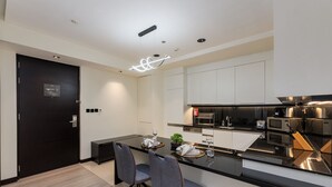 Una cocina moderna con encimera negra, electrodomésticos de acero inoxidable y una zona de comedor con dos sillas y una mesa.