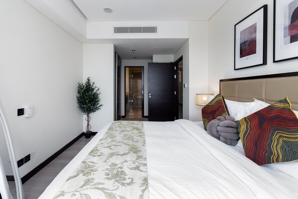 Une chambre d’hôtel avec un grand lit, une tête de lit, une plante en pot et des œuvres d’art encadrées accrochées au mur.