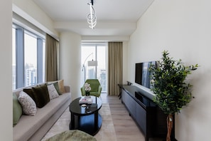 Un salon moderne avec un canapé, une table basse, un téléviseur et une grande fenêtre avec des rideaux.