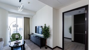 Una habitación de hotel moderna con un ventanal grande, un sillón verde, un mueble de entretenimiento negro y una planta en maceta.