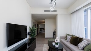 Una sala de estar moderna con un televisor de pantalla plana, una mesa de centro negra, un sofá con almohadones decorativos y una planta.