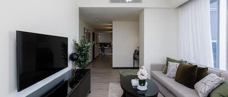 Un salon moderne avec un téléviseur à écran plat, une table basse noire, un canapé agrémenté de coussins décoratifs et une plante.