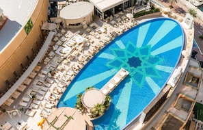 Vue aérienne d’un complexe hôtelier doté d’une grande piscine de forme ovale, de chaises longues et d’un espace bar.