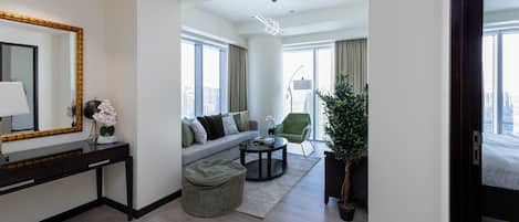 Une chambre d’hôtel moderne avec un canapé, une table basse ronde, un petit pouf, un bureau avec un miroir et une plante en pot.
