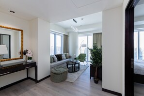A modern hotel room with a sofa, a round coffee table, a small ottoman, a desk with a mirror, and a potted plant. - Chic 1BR in Dubai Marina w/ Direct Mall Access (Dubai)