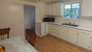 A compact kitchen with white cabinets, a microwave, and a sink. There is a dining table with chairs and a ceiling fan. - Creekfront 3-bedroom house with WiFi, AC in Happy Camp (Happy Camp)