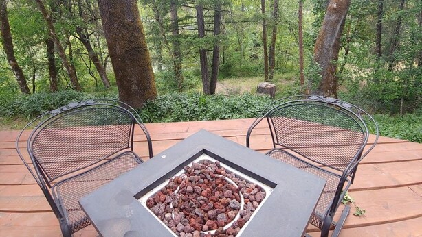A metal table and two chairs on a wooden deck surrounded by trees. - Creekfront 3-bedroom house with WiFi, AC in Happy Camp (Happy Camp)