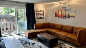 Een moderne woonkamer met een hoekbank, een salontafel en een groot raam met uitzicht op een balkon.