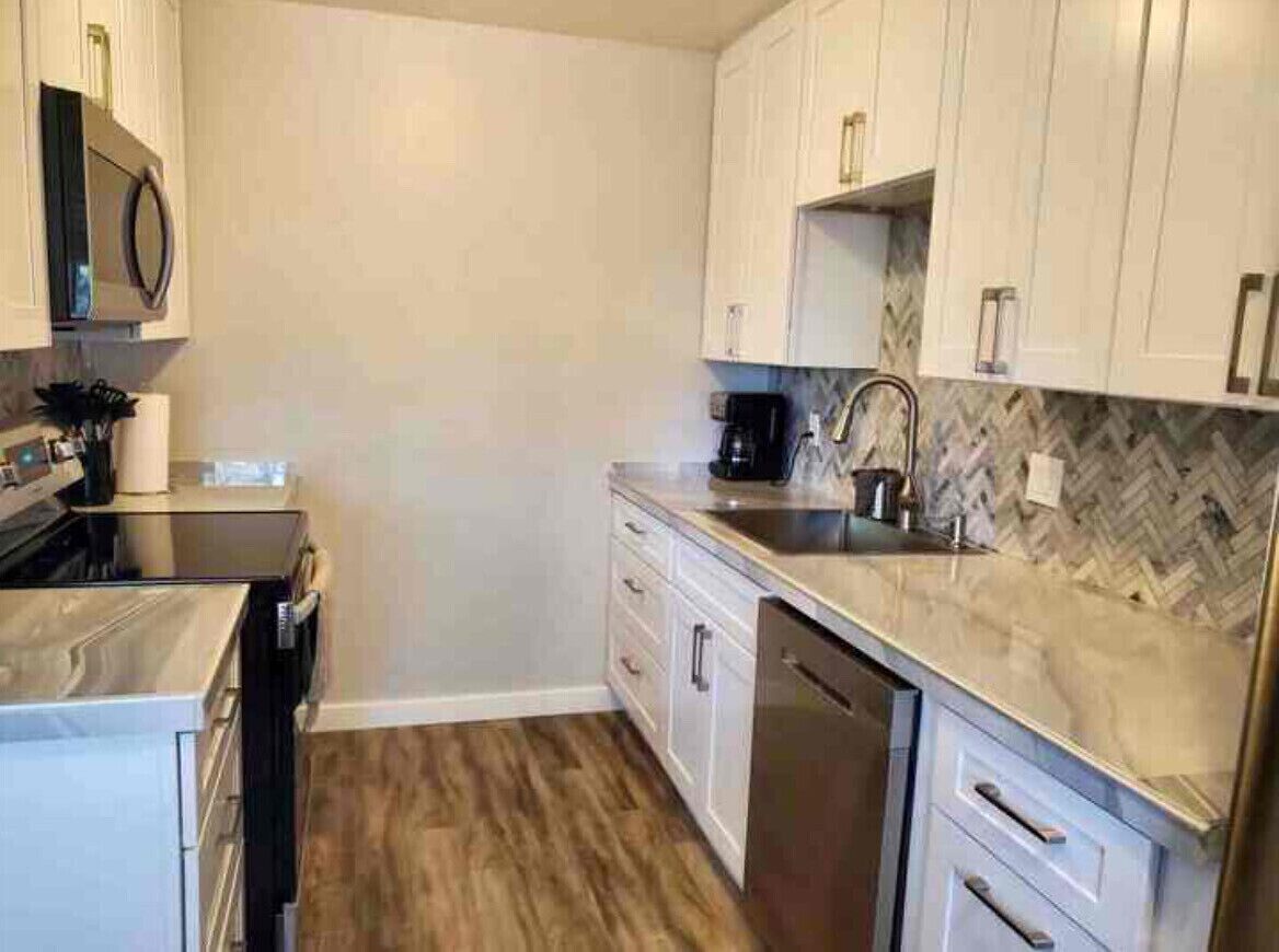 A modern kitchen with white cabinets, a herringbone-patterned backsplash, a stainless steel sink, and a dishwasher.