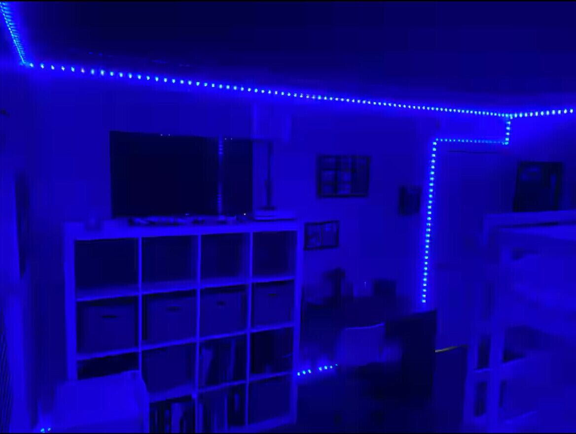 A room with a white shelving unit, a flat-screen TV on top, and a blue LED light strip along the ceiling.