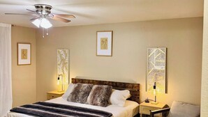Ein Schlafzimmer mit Bett, Nachttischen, einem Sessel, einer Bank, einem Deckenventilator und Bildern an den Wänden.