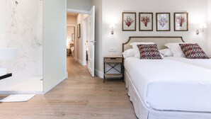Une chambre d’hôtel avec une salle de bain en marbre, un lit agrémenté d’oreillers à motifs et des œuvres d’art encadrées accrochées au mur.