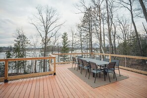 A wooden deck with a table and chairs overlooking a body of water and trees. - Modern 4-bedroom container home on Long Lake! (Sarona)