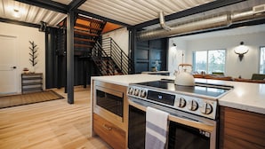 Una cocina moderna con horno empotrado, placa de cocina y una isla grande. Se ve una escalera que sube a un nivel superior.
